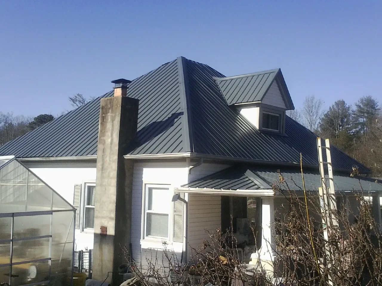 Dark blue standing seam metal roof on a white farmhouse with dormer — Slate & Tile Roof Repair by Roofing Brothers in Pearblossom