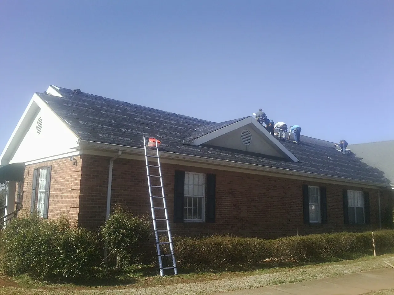 Crew tearing shingles off a brick ranch roof with a ladder set — Metal Roof Repair work by our crew in Pearblossom