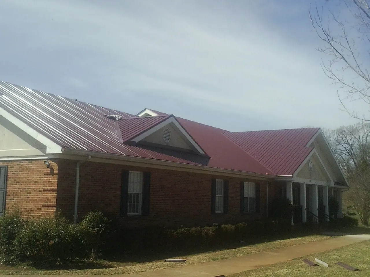 Red metal roof with gabled entries on a long brick building, from a Hail Damage Roof Repair job in Pearblossom