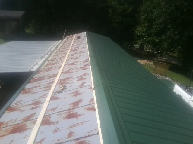 Old rusted panels beside newly installed green metal roofing — Wind Damage Roof Repair by Roofing Brothers in Pearblossom