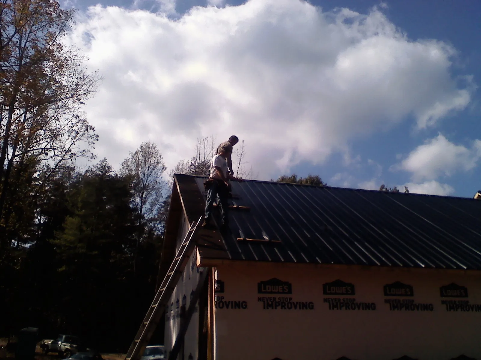 Roofer fastening dark metal panels high against a cloudy sky, from a Roof Inspection job in Pearblossom