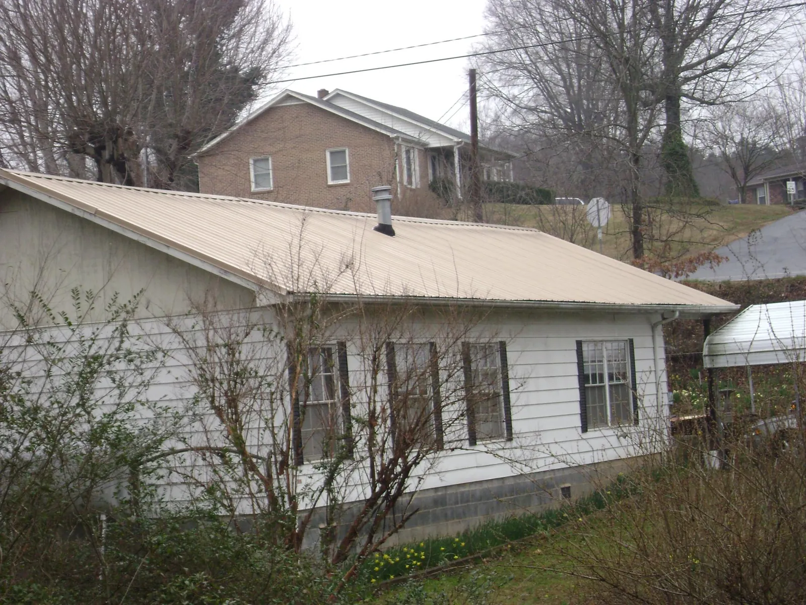 Tan metal roof on a white sided house set into a hillside — Commercial Roofing by Roofing Brothers in Pearblossom
